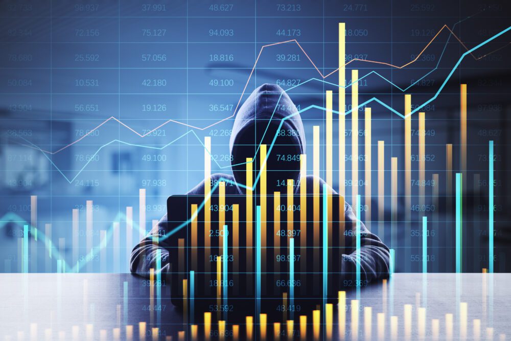 Hacker behind a laptop with financial data charts in the foreground, representing cybercrime in the financial sector.