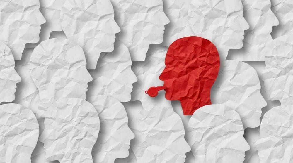 An individual whistleblower profile in red among a crowd of white paper human head shapes.